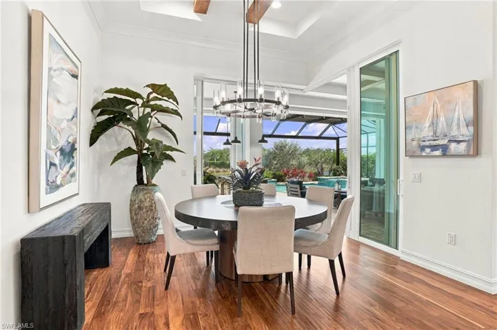 Dining area featuring wood-finish flooring, tray ceiling with exposed wood beams, and a tiered metal chandelier
