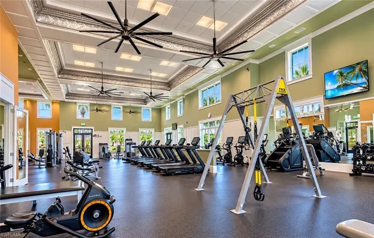 Fitness center featuring decorative tray ceilings with crown molding, expansive ceiling fans, multiple windows, and rubberized flooring
