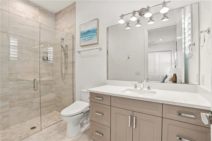 Bathroom featuring a walk-in shower with floor-to-ceiling tile, frameless glass enclosure, vanity with stone countertop, integrated undermount sink, and polished nickel fixtures