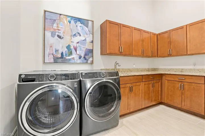 Utility space featuring wood-finish cabinetry, stone-style countertops, an undermount sink with a gooseneck faucet, and tile flooring