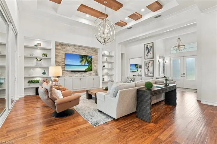 Coffered ceiling with wood-finish inserts, stacked stone fireplace surround, built-in cabinetry with integrated shelving, wood-finish flooring, and multi-arm orb chandelier