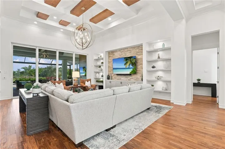 Coffered ceiling with wood-toned accents, stone-clad media wall, built-in shelving, multi-panel sliding glass doors, and wood-finish flooring