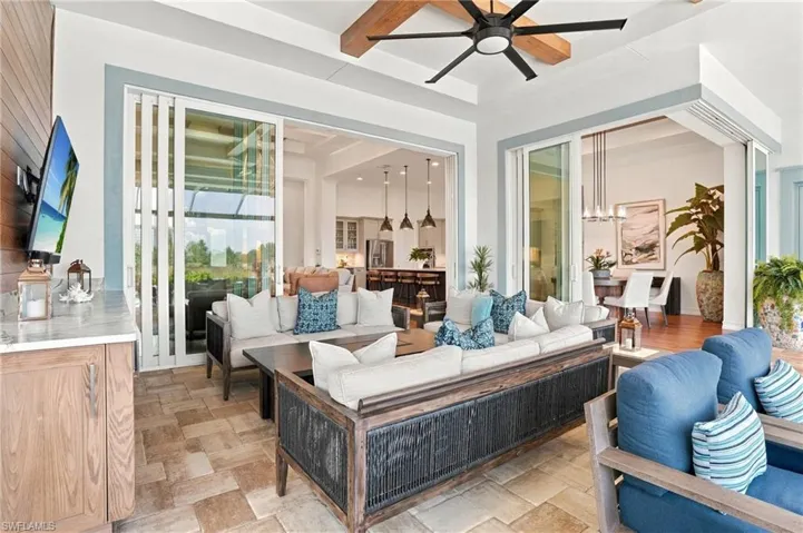 Covered patio featuring stone-tile flooring, ceiling beam detail, built-in cabinetry with stone countertop, and multi-panel sliding glass doors