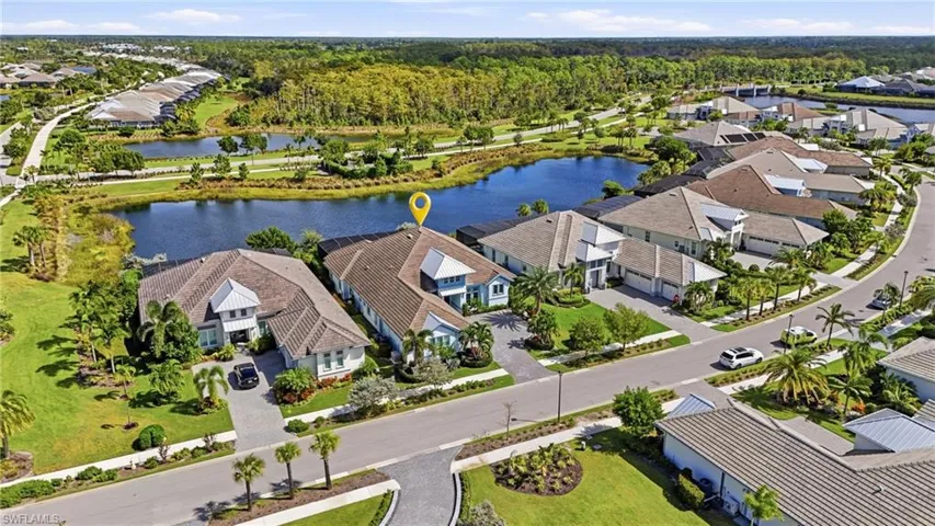 Aerial perspective featuring a waterfront property with a tile roof, paved driveway, and screened-in rear lanai