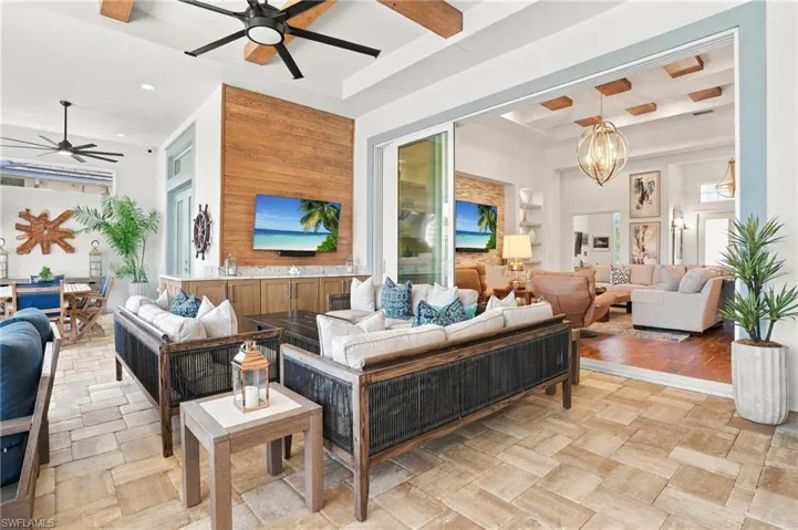 Covered patio featuring paver flooring, wood-paneled accent wall with built-in cabinetry, exposed ceiling beams, and a multi-panel sliding glass door system