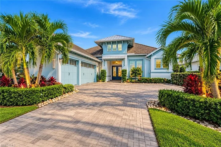 Exterior facade featuring light blue siding, a paver driveway, three-car garage, and formal landscaping
