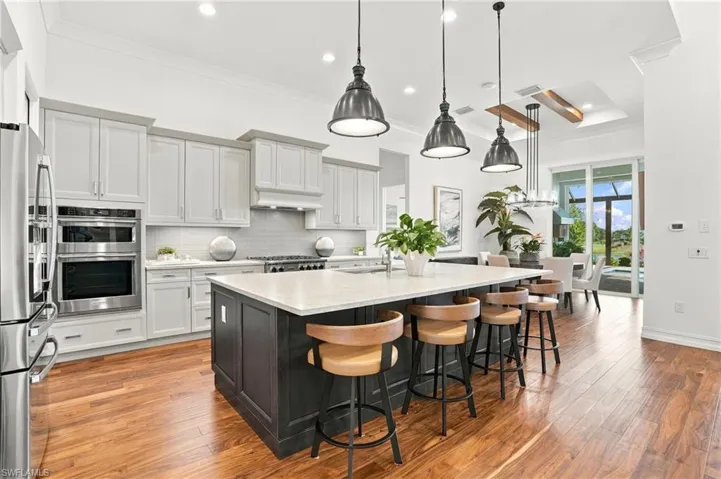 Kitchen featuring a large central island with quartz countertops, custom cabinetry, stainless steel double wall ovens, wood-finish flooring, and pendant lighting