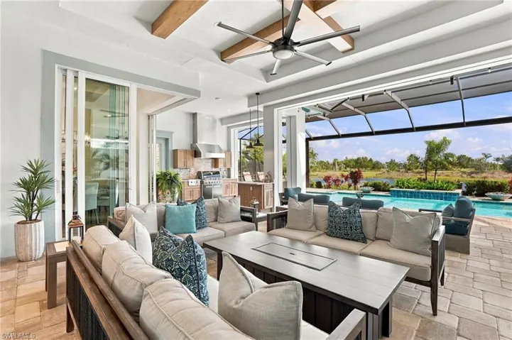 Covered lanai featuring exposed wood ceiling beams, a built-in outdoor kitchen, stone-paver flooring, multi-panel sliding glass doors, and a screened enclosure overlooking the swimming pool