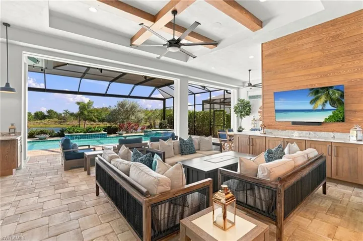 Covered lanai featuring paver flooring, wood-paneled accent wall with built-in cabinetry, exposed wood ceiling beams, and a screened enclosure opening to an inground pool