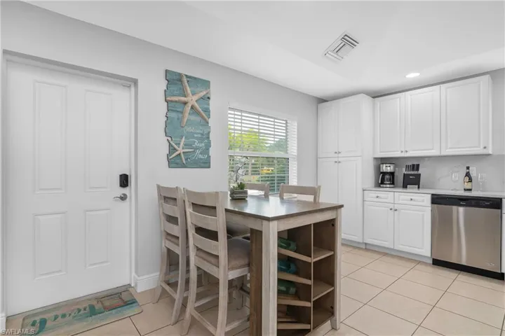 Kitchen with dishwasher, light tile patterned floors, backsplash, and white cabinets