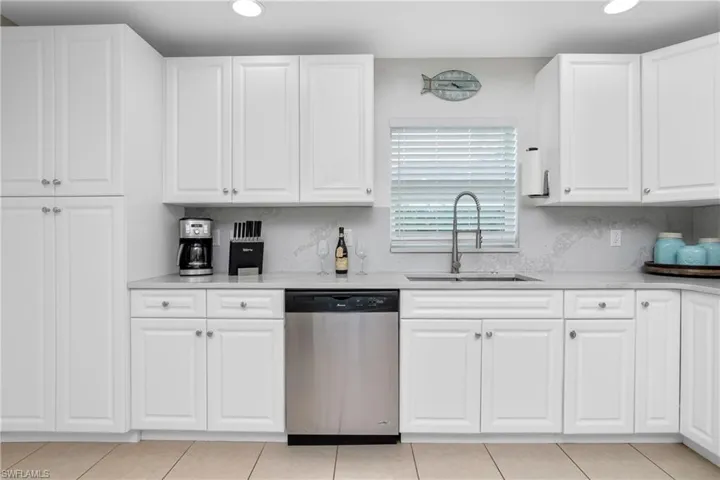Kitchen featuring dishwasher, light tile patterned floors, white cabinetry, and sink