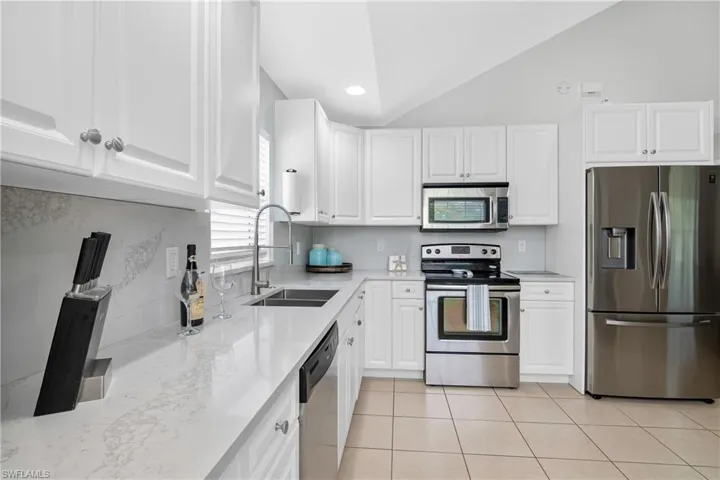 Kitchen with white cabinetry, appliances with stainless steel finishes, vaulted ceiling, and sink