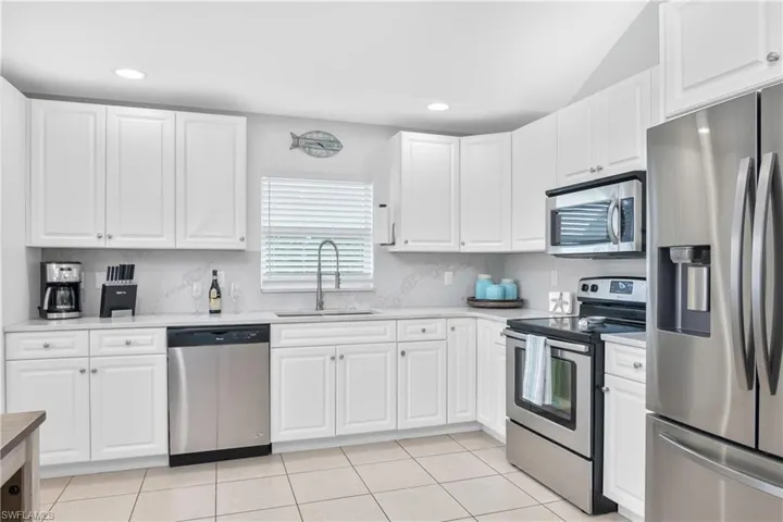 Kitchen featuring sink, appliances with stainless steel finishes, white cabinetry, and light tile patterned flooring