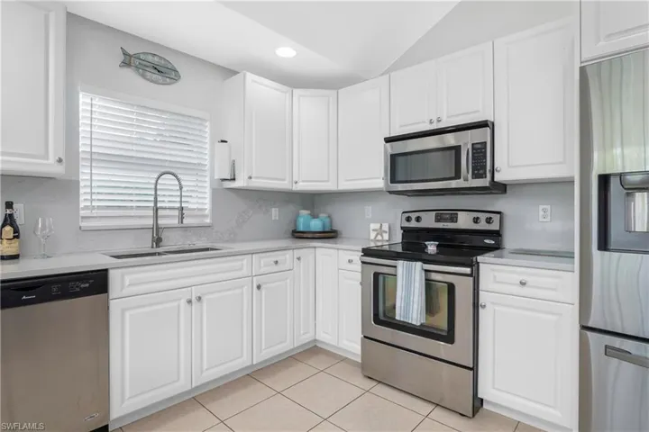 Kitchen featuring white cabinets, light tile patterned floors, vaulted ceiling, stainless steel appliances, and sink