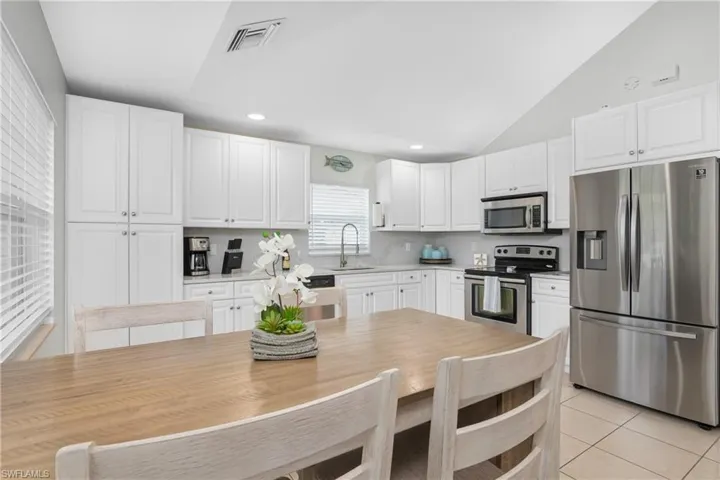 Kitchen featuring vaulted ceiling, white cabinetry, stainless steel appliances, and sink