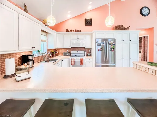 Kitchen with a kitchen bar, backsplash, hanging light fixtures, and white appliances