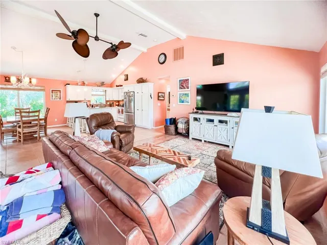 Living room featuring vaulted ceiling with beams, light tile patterned floors, and ceiling fan with notable chandelier
