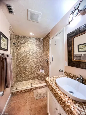 Bathroom with tiled shower, a textured ceiling, vanity, and tile patterned flooring
