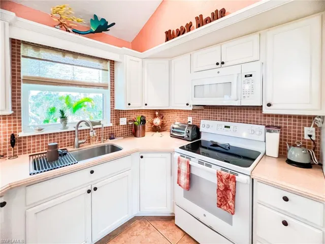 Kitchen featuring lofted ceiling, white appliances, sink, light tile patterned floors, and white cabinetry