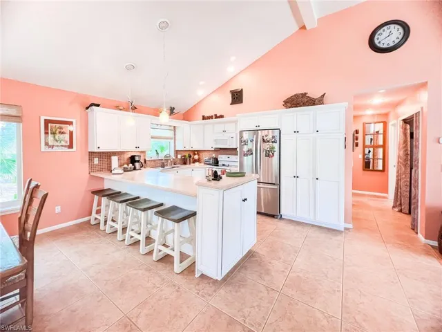 Kitchen featuring decorative backsplash, stainless steel fridge, sink, decorative light fixtures, and white cabinets