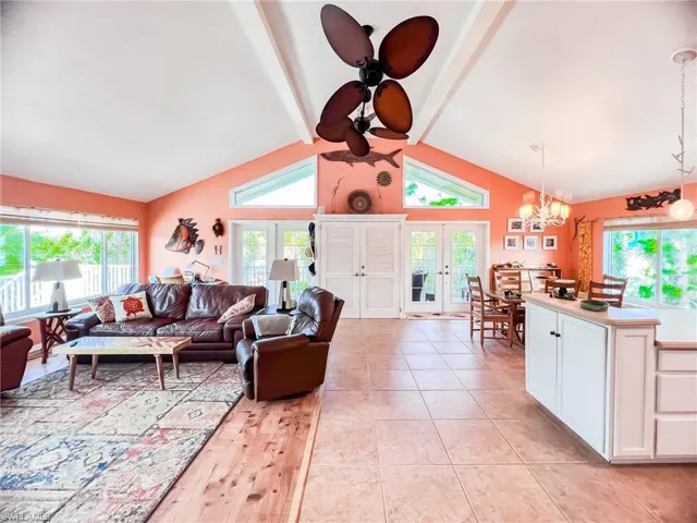 Living room featuring ceiling fan with notable chandelier, french doors, lofted ceiling with beams, and light tile patterned floors
