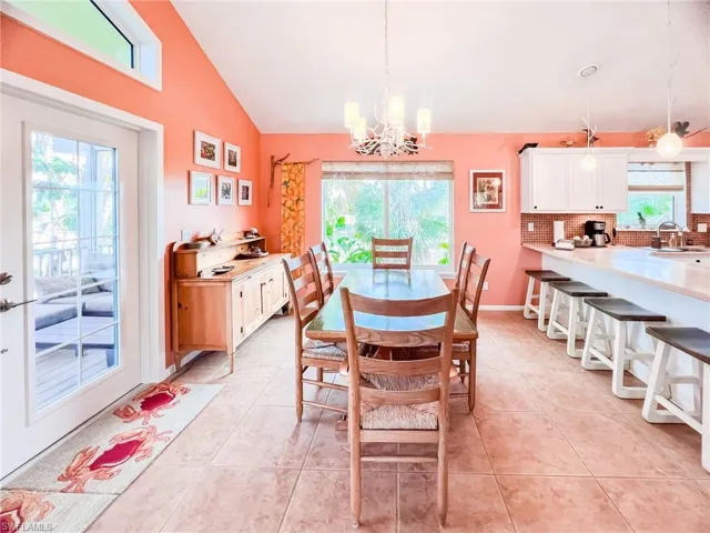 Dining room featuring sink, light tile patterned flooring, vaulted ceiling, and a notable chandelier
