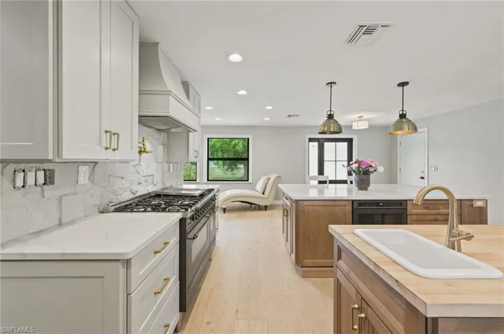 Kitchen with double oven range, a center island with sink, custom exhaust hood, light wood-type flooring, and tasteful backsplash