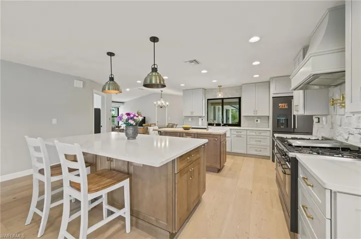 Kitchen with high end appliances, premium range hood, a large island, light wood-style floors, and backsplash