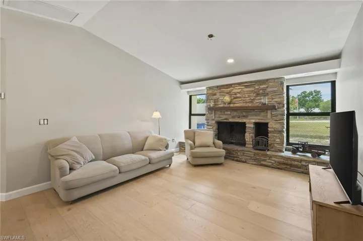 Living area with light wood-style flooring, vaulted ceiling, a stone fireplace, and recessed lighting
