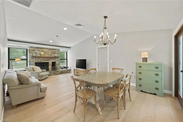 Dining area featuring light wood-type flooring, a chandelier, lofted ceiling, a fireplace, and recessed lighting
