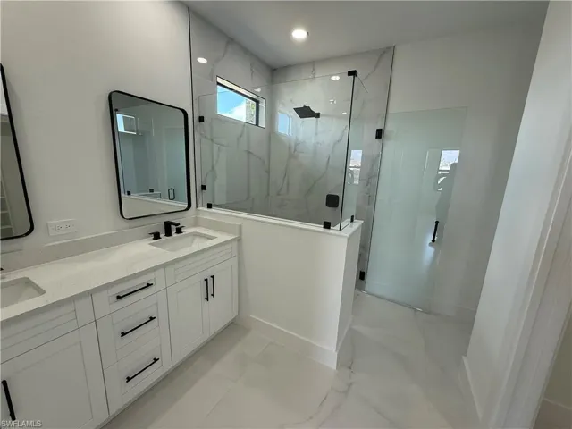 Bathroom featuring double vanity, marble finish floor, a sink, and a marble finish shower