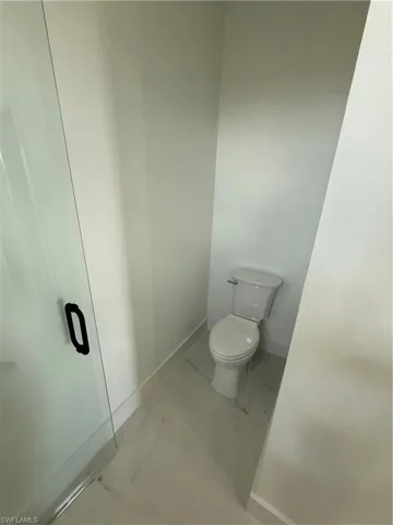 Bathroom featuring toilet, marble finish floor, and baseboards