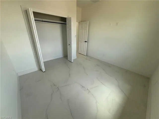 Unfurnished bedroom with a closet, baseboards, and marble finish floor