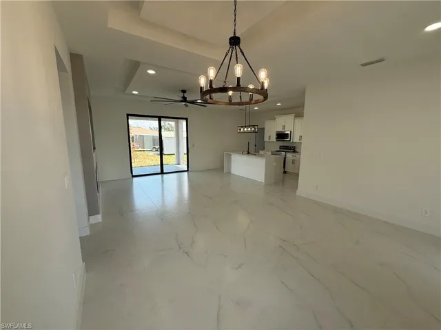 Unfurnished dining area featuring baseboards, a raised ceiling, an inviting chandelier, recessed lighting, and marble finish floor