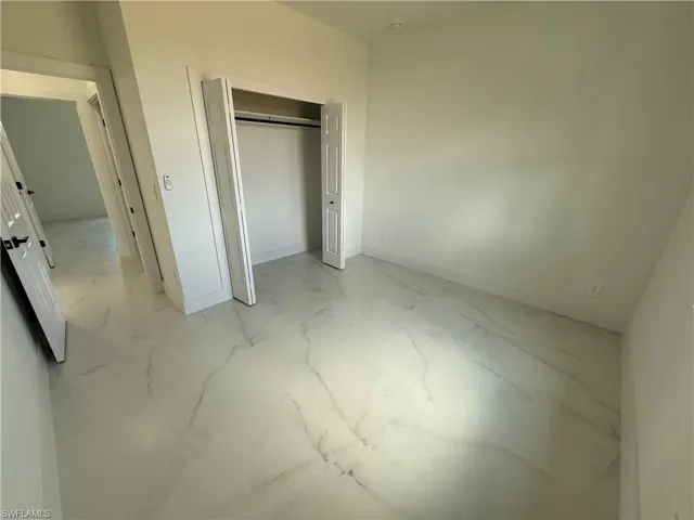 Unfurnished bedroom with a closet, marble finish floor, and baseboards