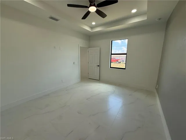 Empty room with marble finish floor, a tray ceiling, and baseboards
