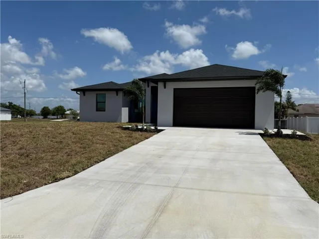 View of front of home with concrete driveway, stucco siding, a front lawn, a garage, and fence