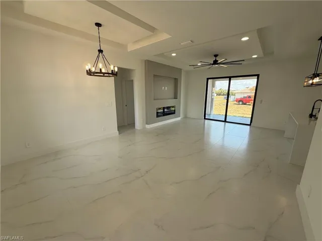 Unfurnished living room with baseboards, a tray ceiling, recessed lighting, ceiling fan with notable chandelier, and marble finish floor