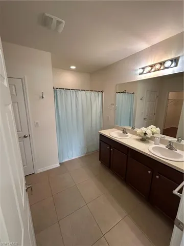 Full bath with double vanity, light tile patterned floors, curtained shower, and recessed lighting