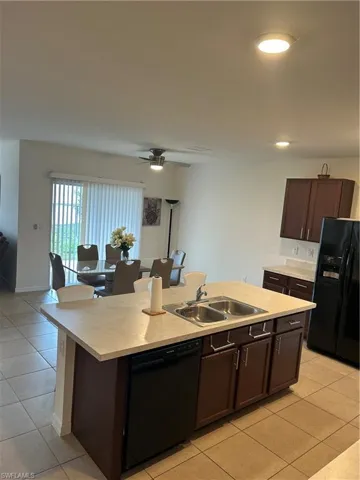 Kitchen featuring dark wood finish cabinetry, light countertops, black refrigerator, and dishwashing machine
