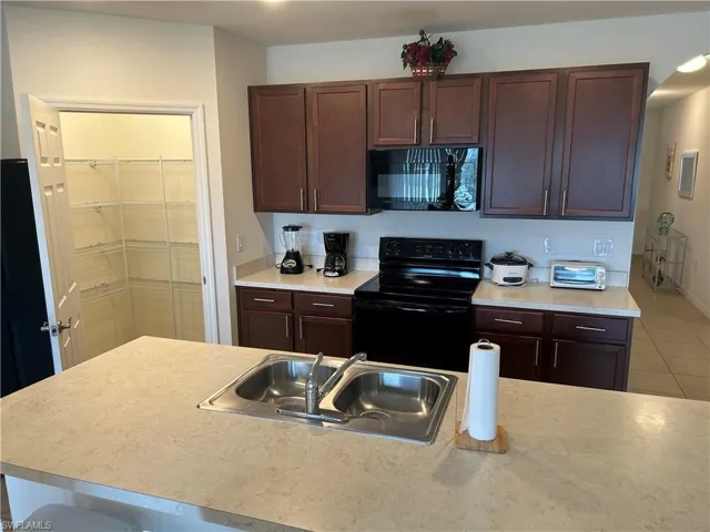 Kitchen with light countertops, black appliances, and dark wood finish cabinetry