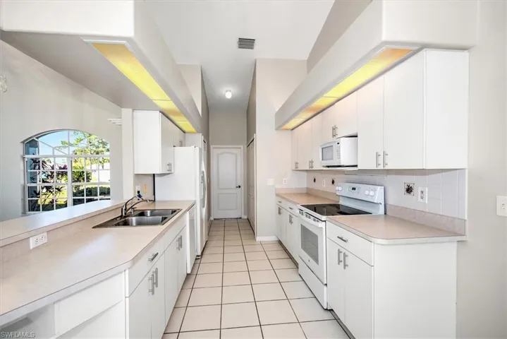 Kitchen with tasteful backsplash, white appliances, sink, light tile patterned floors, and white cabinets