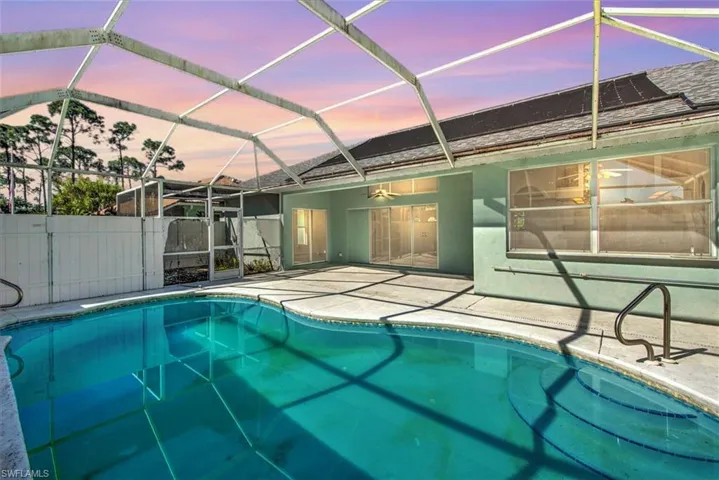 Pool at dusk with glass enclosure, ceiling fan, and a patio area