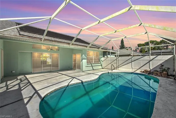 Pool at dusk with ceiling fan, a patio area, and glass enclosure