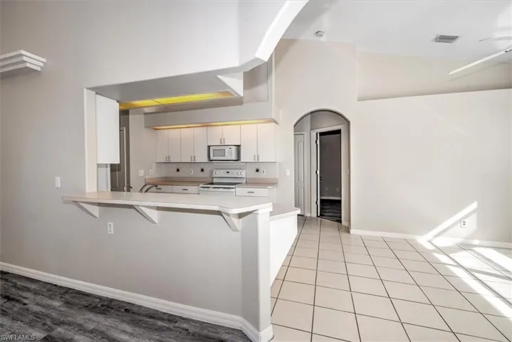 Kitchen with white cabinets, a kitchen bar, white appliances, and kitchen peninsula