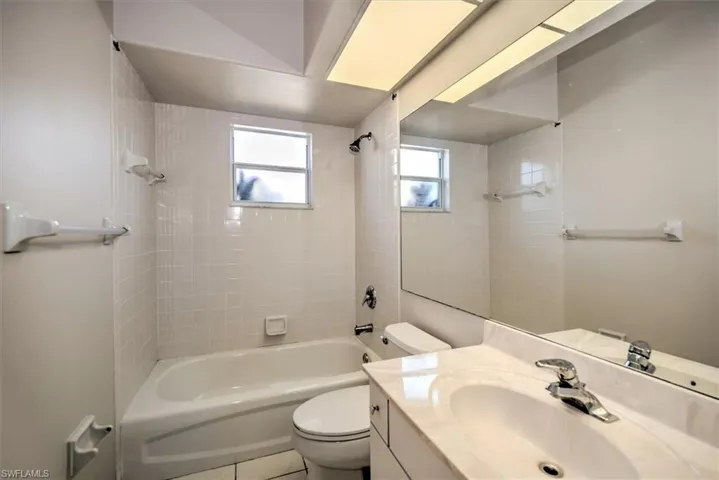 Full bathroom with vanity, tile patterned floors, tiled shower / bath combo, and toilet