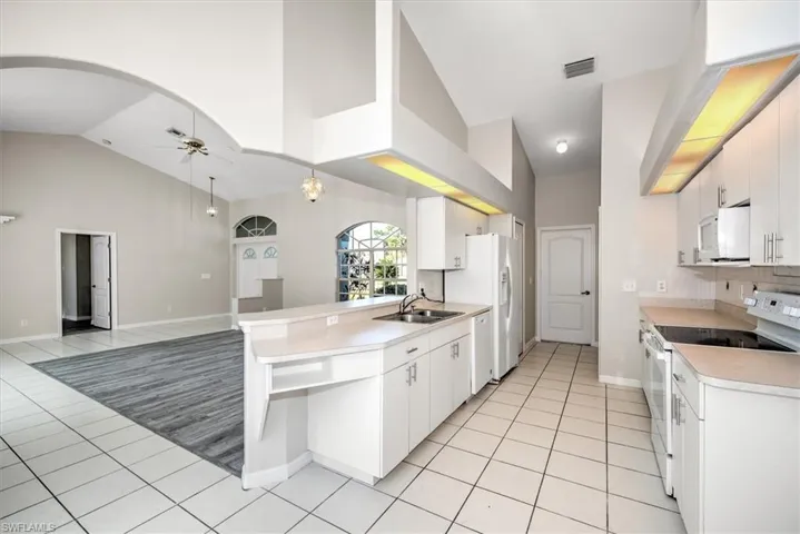 Kitchen featuring white appliances, white cabinets, sink, ceiling fan, and light tile patterned floors