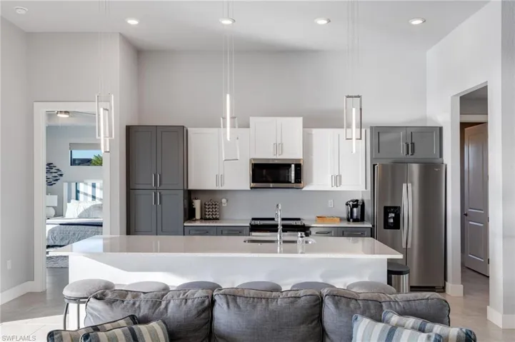 Kitchen with appliances with stainless steel finishes, gray cabinetry, light stone countertops, recessed lighting, and a center island with sink