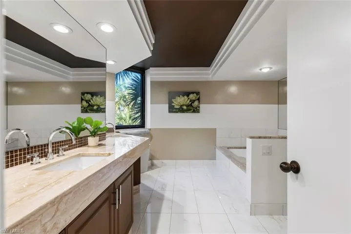 Bathroom with vanity, a raised ceiling, ornamental molding, and tiled tub