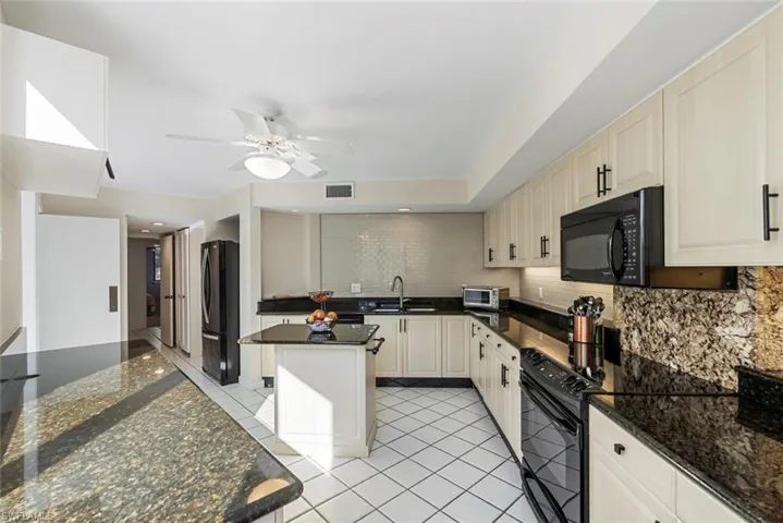 Kitchen featuring black appliances, sink, decorative backsplash, dark stone countertops, and a kitchen island